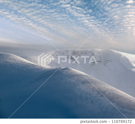 Snow covered winter mountains  in last evening sunlight. Magnificent windy dusk on tops above picturesque alpine ski resort 110789172