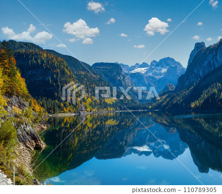 Peaceful autumn Alps mountain lake with clear transparent water and reflections. Gosauseen or Vorderer Gosausee lake, Upper Austria. Dachstein summit and glacier in far. 110789305