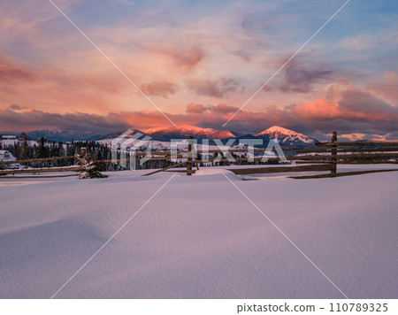 Alpine village outskirts in last evening sunset sun light. Winter snowy hills and fir trees. Alpine village outskirts in last evening sunset sun light. Winter snowy hills and fir trees. 110789325