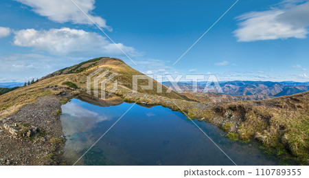 Small picturesque lake with clouds reflections at the  Strymba Mount. Beautiful autumn day in Carpathian Mountains near Kolochava village, Transcarpathia, Ukraine. 110789355