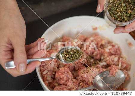 Woman's hands pouring seasoning into meat close-up. The process of cooking meat. 110789447