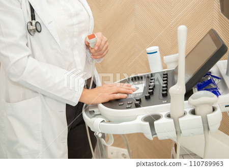 Close-up of Gynecologist doctor hand with high-tech ultrasound machine with backlight. Close-up of Gynecologist doctor hand with high-tech ultrasound machine with backlight. 110789963