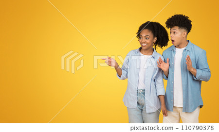 A young woman and man in casual attire are excitedly pointing to something off-camera 110790378