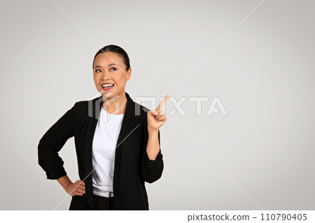 Enthusiastic Asian businesswoman with a beaming smile pointing upwards 110790405