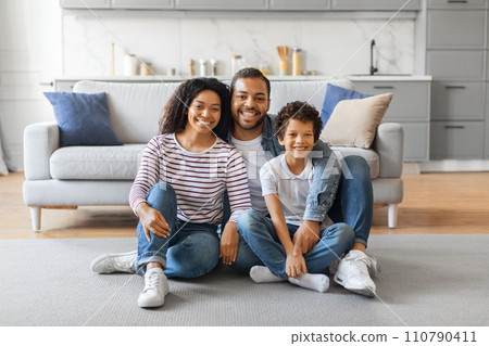 Smiling black family with son sitting on floor in cozy living room Smiling black family with son sitting on floor in cozy living room 110790411