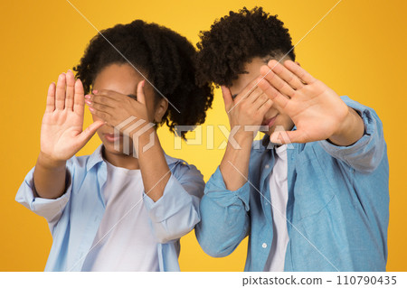 Two young individuals, a girl and a boy, playfully enact 'see no evil' with hands over eyes 110790435