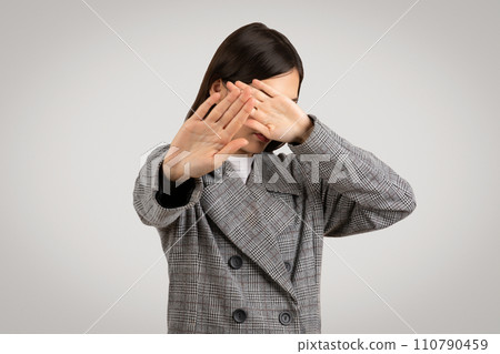 Young woman in houndstooth coat, covering face with hands 110790459
