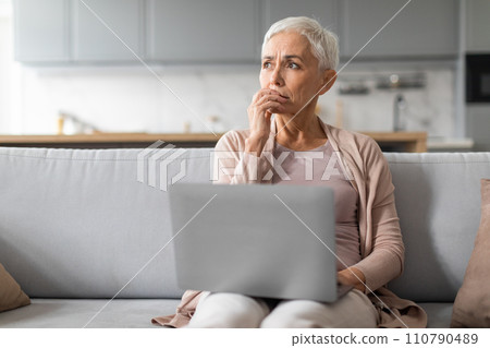 Concerned mature lady working on laptop thinking about issues indoor Concerned mature lady working on laptop thinking about issues indoor 110790489