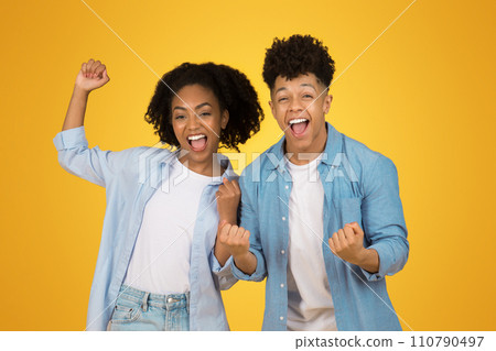 Two exuberant young adults celebrate with raised fists and bright smiles 110790497