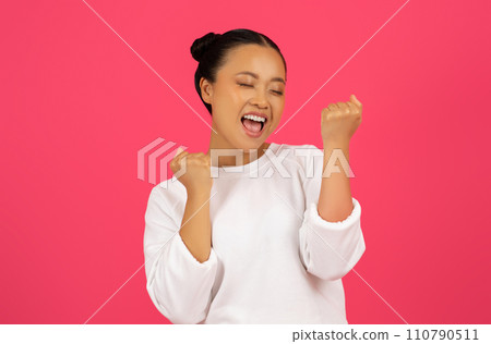 Joyful young asian woman clenching fists and celebrating success Joyful young asian woman clenching fists and celebrating success 110790511