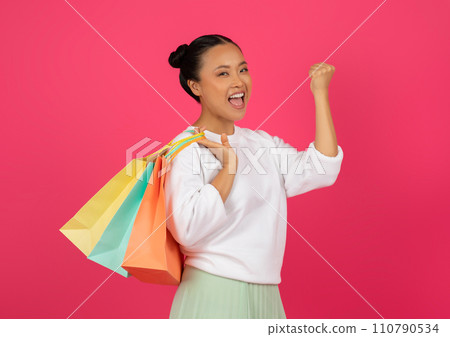 Big Discounts. Happy young asian woman carrying shopping bags and shaking fist Big Discounts. Happy young asian woman carrying shopping bags and shaking fist 110790534