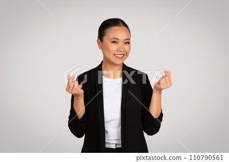 Optimistic Asian businesswoman in a black blazer making a wishful fingers crossed gesture with a hopeful smile 110790561