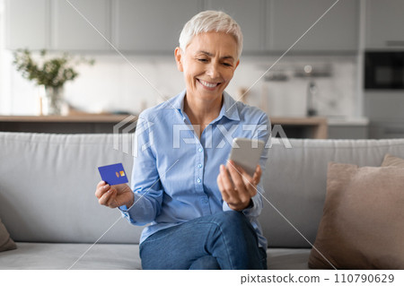 mature woman shopping online using phone holding credit card indoor mature woman shopping online using phone holding credit card indoor 110790629