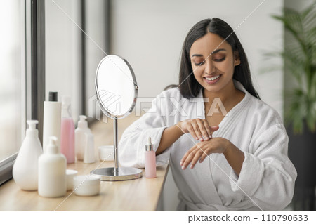 Happy young indian woman enjoying her morning face care routine Happy young indian woman enjoying her morning face care routine 110790633