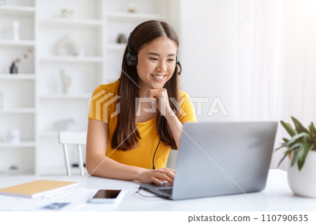 Focused asian woman wearing headset working on her laptop in home office 110790635