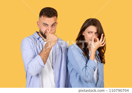Disgusted couple pinching noses, displeased faces on yellow background 110790704