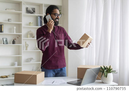 Young Indian Businessman Holding Packed Box With Order And Talking On Cellphone Young Indian Businessman Holding Packed Box With Order And Talking On Cellphone 110790735