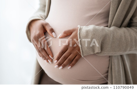 Pregnant black woman holding palms in heart shape on tummy Pregnant black woman holding palms in heart shape on tummy 110790849