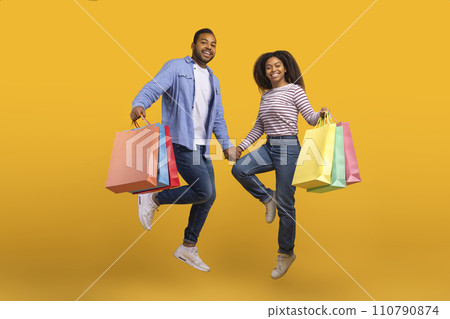 Cheerful Black Couple Holding Hands And Jumping With Shopping Bags 110790874