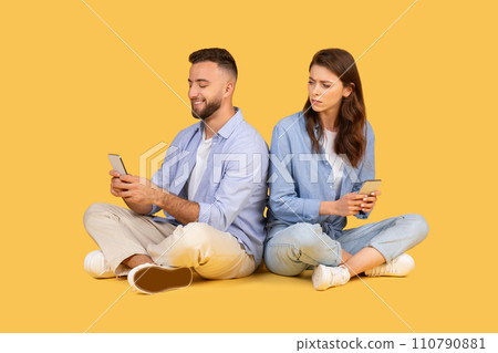 Man and woman sitting back-to-back, focused on their smartphones 110790881
