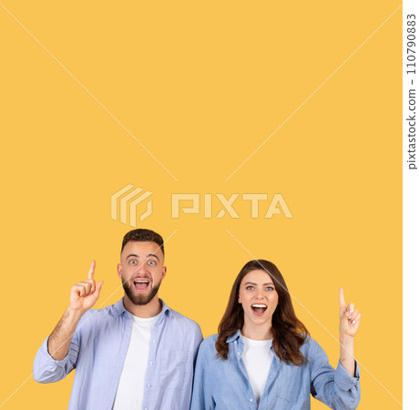 Excited couple pointing upwards at free space, having an aha-moment on yellow background Excited couple pointing upwards at free space, having an aha-moment on yellow background 110790883