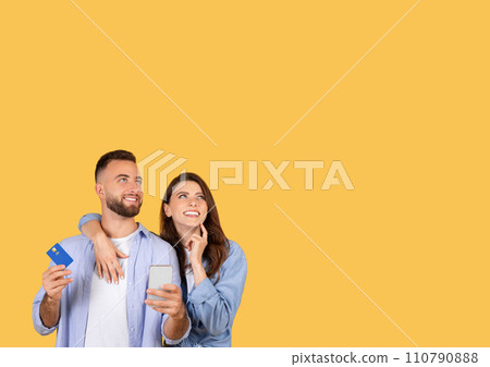 Couple planning purchase with credit card and phone, optimistic on yellow, free space 110790888