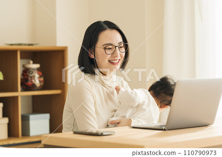 A woman working from home while holding a baby 110790973