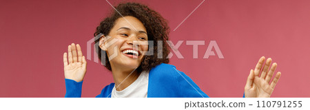 Happy woman in casual clothes dancing with raised hands while standing over red studio background 110791255