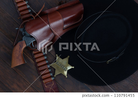 Marshal star with gun, holster and gun belt with old west hat on table. Top view. 110791455