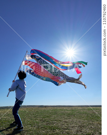 A boy holding up a carp streamer under the blue sky A boy holding up a carp streamer under the blue sky 110792460
