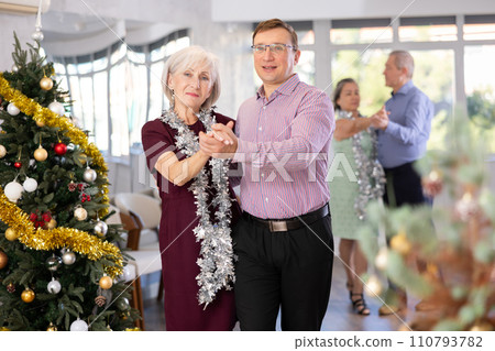 Active middle-aged man and mature woman in pair practicing ballroom dance in training hall during Christmas party 110793782