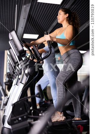 Fit young woman working out at elliptical machine in gym Fit young woman working out at elliptical machine in gym 110793819
