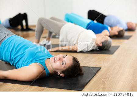 Group of young mature old people in sportswear exercising Pilates while lying on mats in rehabilitation center 110794012