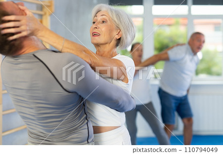 Senior woman in pair with middle-aged coach train Krav Maga and self-defense skills. 110794049