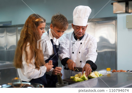 Chef teacher teaches cooking to the group children in class kitchen room.  110794074