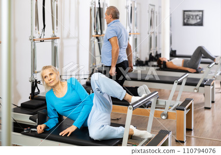 Two female and male training back while working out on Pilates reformer machine bed in studio. Wellbeing and healthy lifestyle concept Two female and male training back while working out on Pilates reformer machine bed in studio. Wellbeing and healthy lifestyle concept 110794076