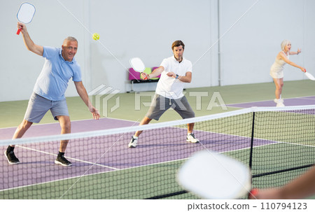 Senior man playing doubles pickleball with male partner indoors Senior man playing doubles pickleball with male partner indoors 110794123