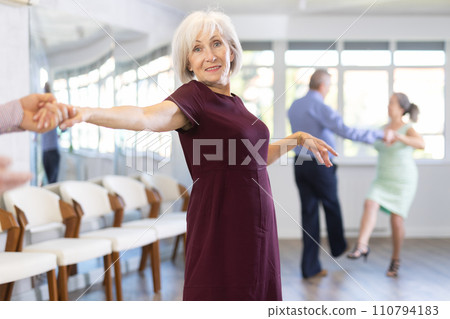 Happy elderly lady with man in elegant clothes dancing bachata in ballroom dance class Happy elderly lady with man in elegant clothes dancing bachata in ballroom dance class 110794183