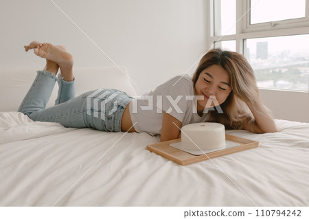 Lovely beautiful happy woman lies on the bed admiring her birthday cake. Lovely beautiful happy woman lies on the bed admiring her birthday cake. 110794242