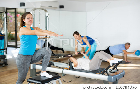 European young woman wearing sportswear performing Pilates exercises on combo chair machine in gym indoors European young woman wearing sportswear performing Pilates exercises on combo chair machine in gym indoors 110794350