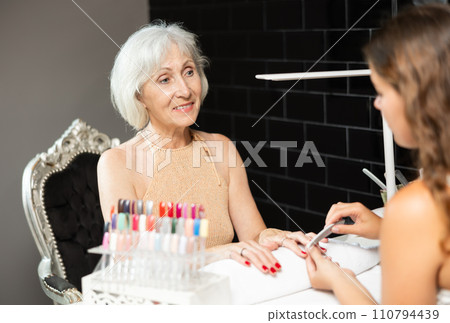 Unrecognizable girl manicure master files nails and performs grooming procedure for senior woman 110794439