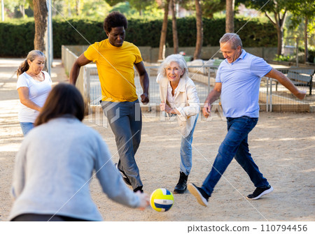 Cheerful males and females kicking the ball in park 110794456