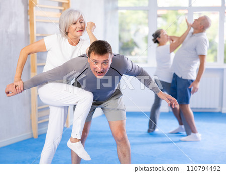 Senior woman in pair with middle-aged coach train Krav Maga and self-defense skills. Senior woman in pair with middle-aged coach train Krav Maga and self-defense skills. 110794492