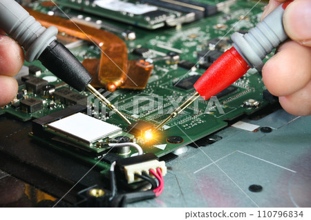 Technician checking electronics part on circuit board with probe of digital multimeter 110796834