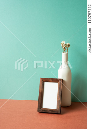Empty wooden picture frame with white vase of dry flower on red table. mint green wall background 110797332