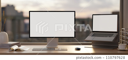 A PC computer and laptop mockup and office supplies on a table against the window with a city view. 110797628