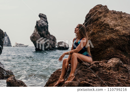 Woman summer travel sea. Happy tourist in blue bikini enjoy taking picture outdoors for memories. Woman traveler posing on the beach surrounded by volcanic mountains, sharing travel adventure journey Woman summer travel sea. Happy tourist in blue bikini enjoy taking picture outdoors for memories. Woman traveler posing on the beach surrounded by volcanic mountains, sharing travel adventure journey 110799216
