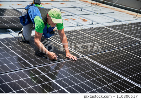 Worker building photovoltaic solar panel system on rooftop of house. Man engineer installing solar module with help of wrench outdoors. Alternative and renewable energy generation concept. 110800517