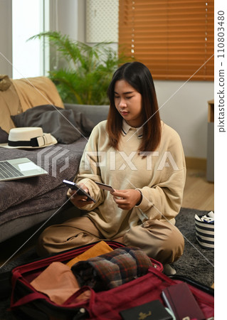 Portrait of young woman booking a trip online on mobile phone with credit card 110803480