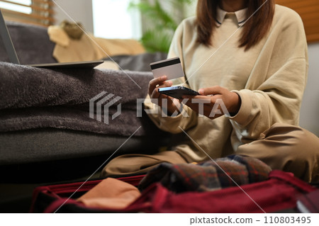 Cropped shot young woman booking online on mobile phone with credit card for holiday 110803495